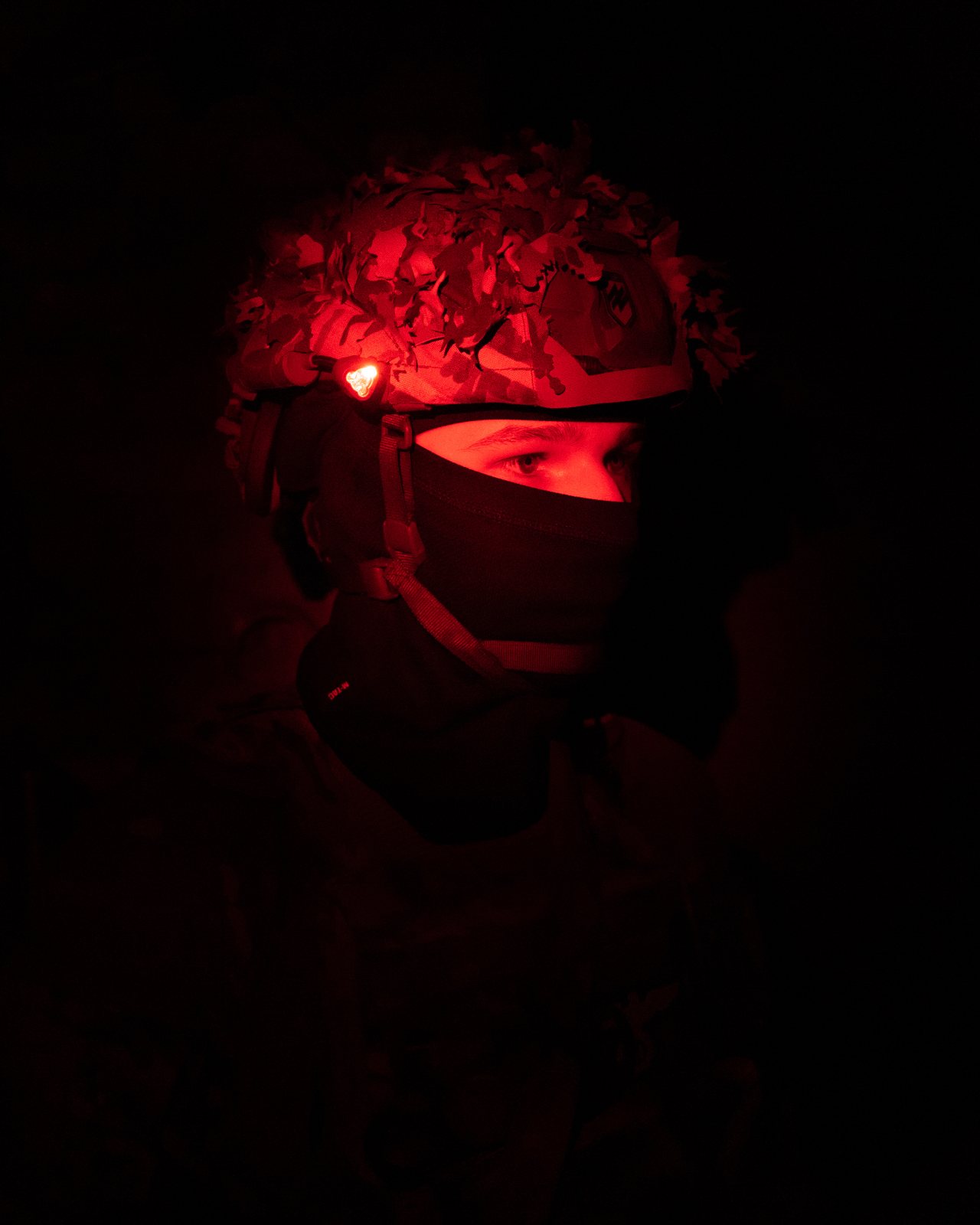 Retrato de un soldado ucraniano iluminado por una luz roja frontal en la oscuridad.