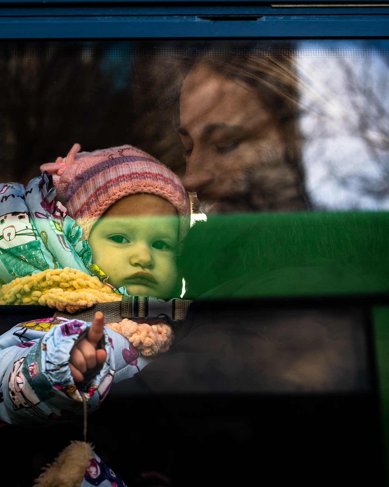 Una madre y su bebé reflejados en la ventana de un autobús de evacuación.